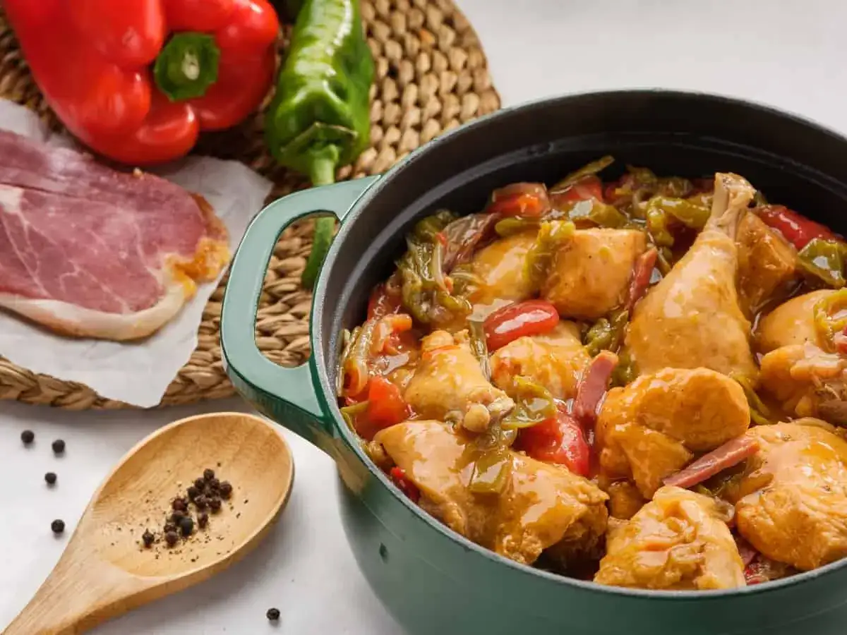 Un delicioso pollo al chilindr&oacute;n en cazuela verde, con pimientos rojos y verdes, jam&oacute;n y granos de pimienta.