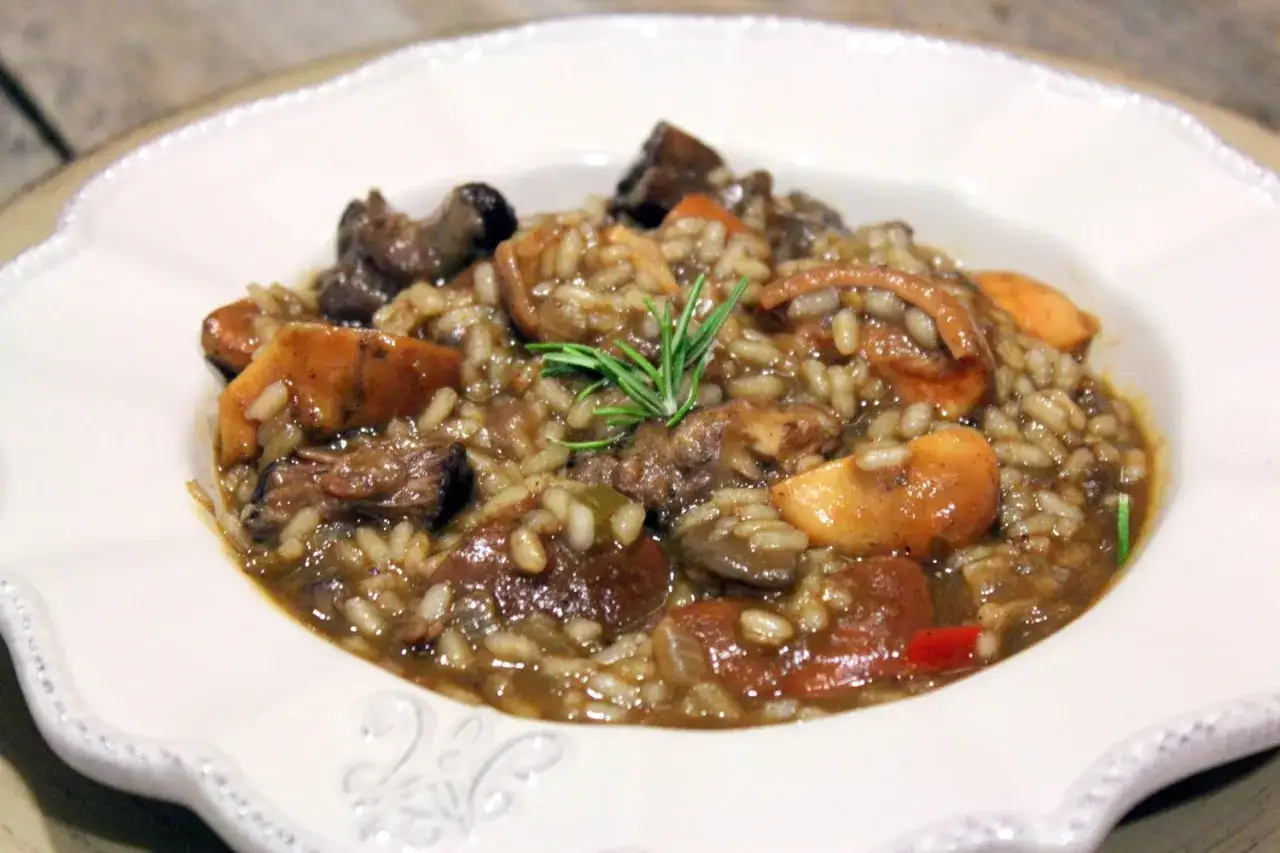Delicioso arroz con niscalos y carne, servido en un plato blanco con un toque de romero.