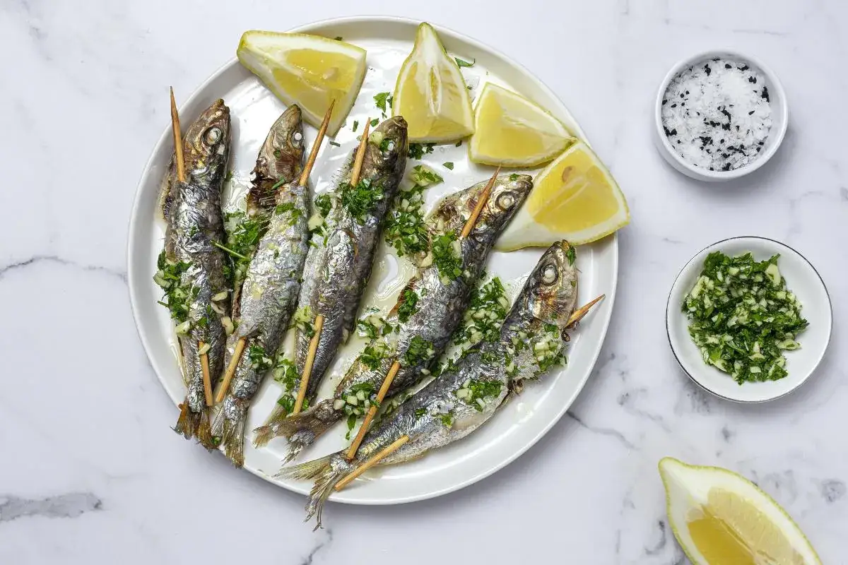 Sardinas al horno en brochetas, servidas con gajos de limón y perejil picado. Un plato sencillo y delicioso.