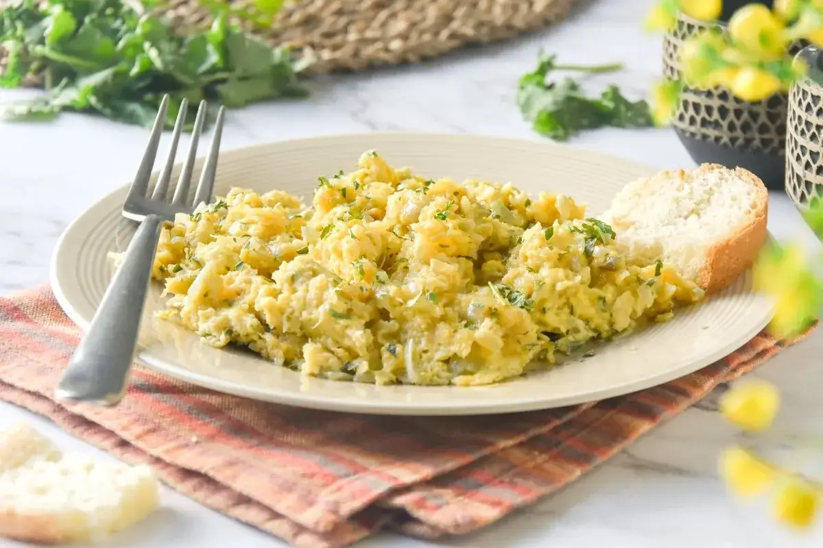 Un delicioso revuelto de bacalao con perejil fresco, servido con pan crujiente y un tenedor listo para disfrutar.