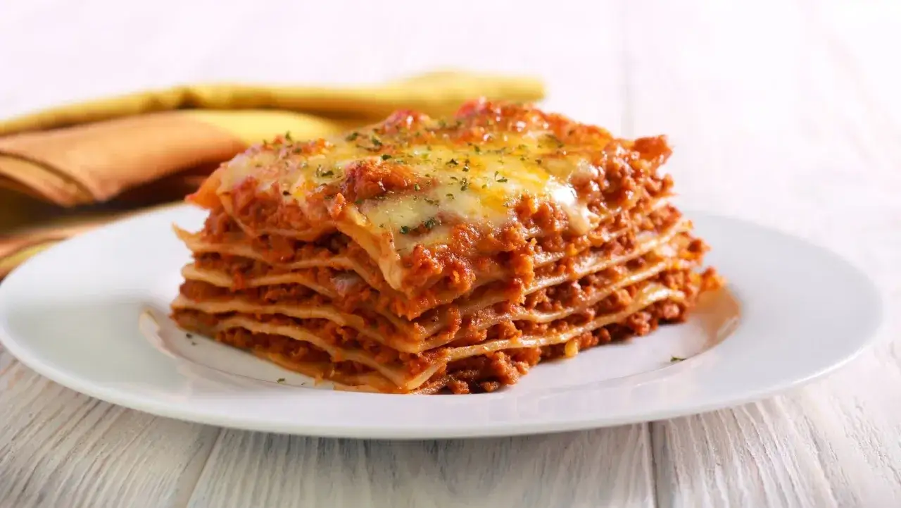 Porci&oacute;n generosa de lasa&ntilde;a de carne, con capas de pasta, salsa bolo&ntilde;esa y queso derretido, servida en un plato blanco.