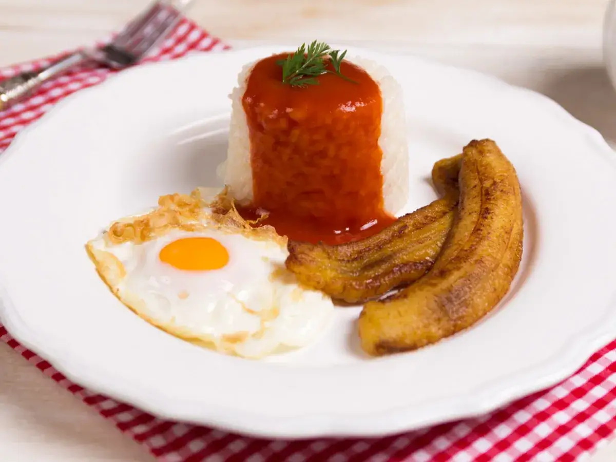 Un plato de arroz a la cubana con huevo frito, plátanos maduros fritos y salsa de tomate.
