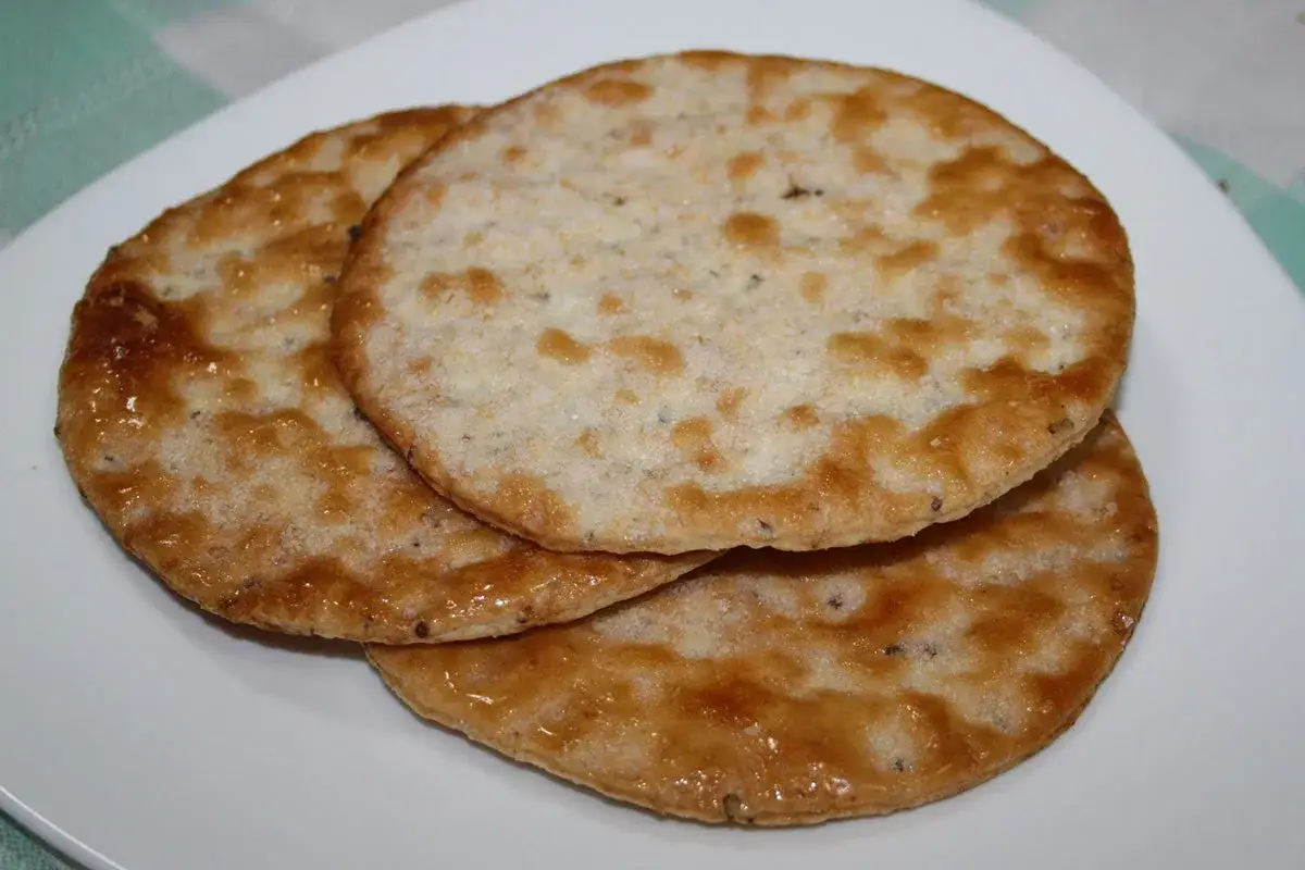 Tres tortas de anís doradas y crujientes apiladas en un plato blanco.
