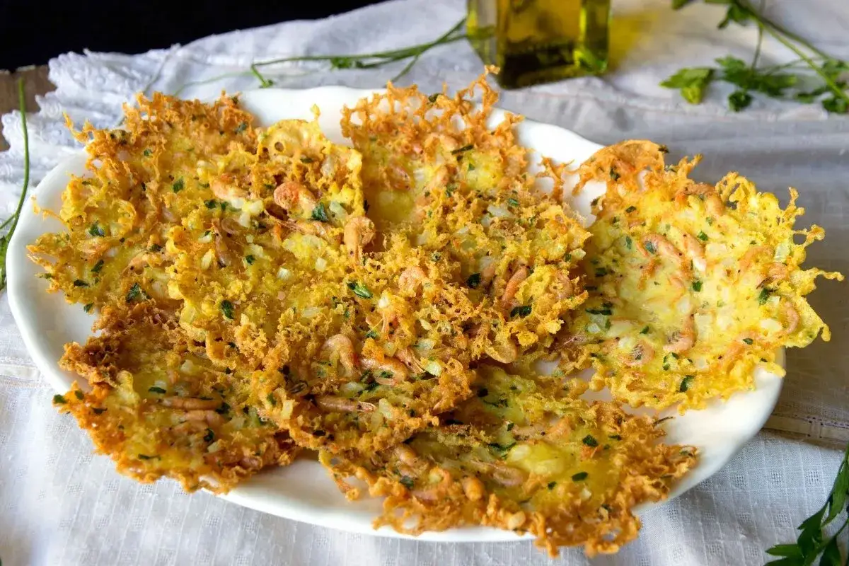 Tortillitas de camarones crujientes y doradas, con pequeños camarones y perejil picado, servidas en un plato blanco.
