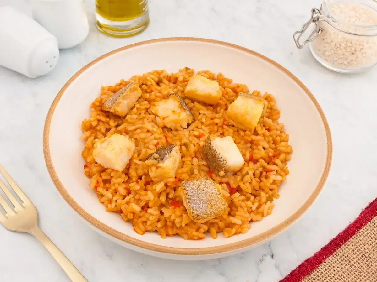 Un delicioso plato de arroz con bacalao, con trozos de pescado blanco sobre un arroz rojizo y sabroso.