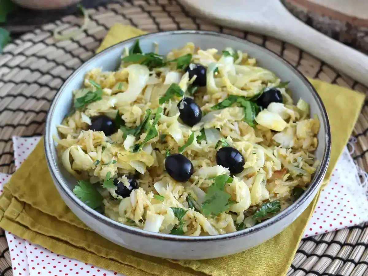 Delicioso bacalao a bras, un plato tradicional con patatas finas, huevo y aceitunas negras, adornado con perejil fresco.