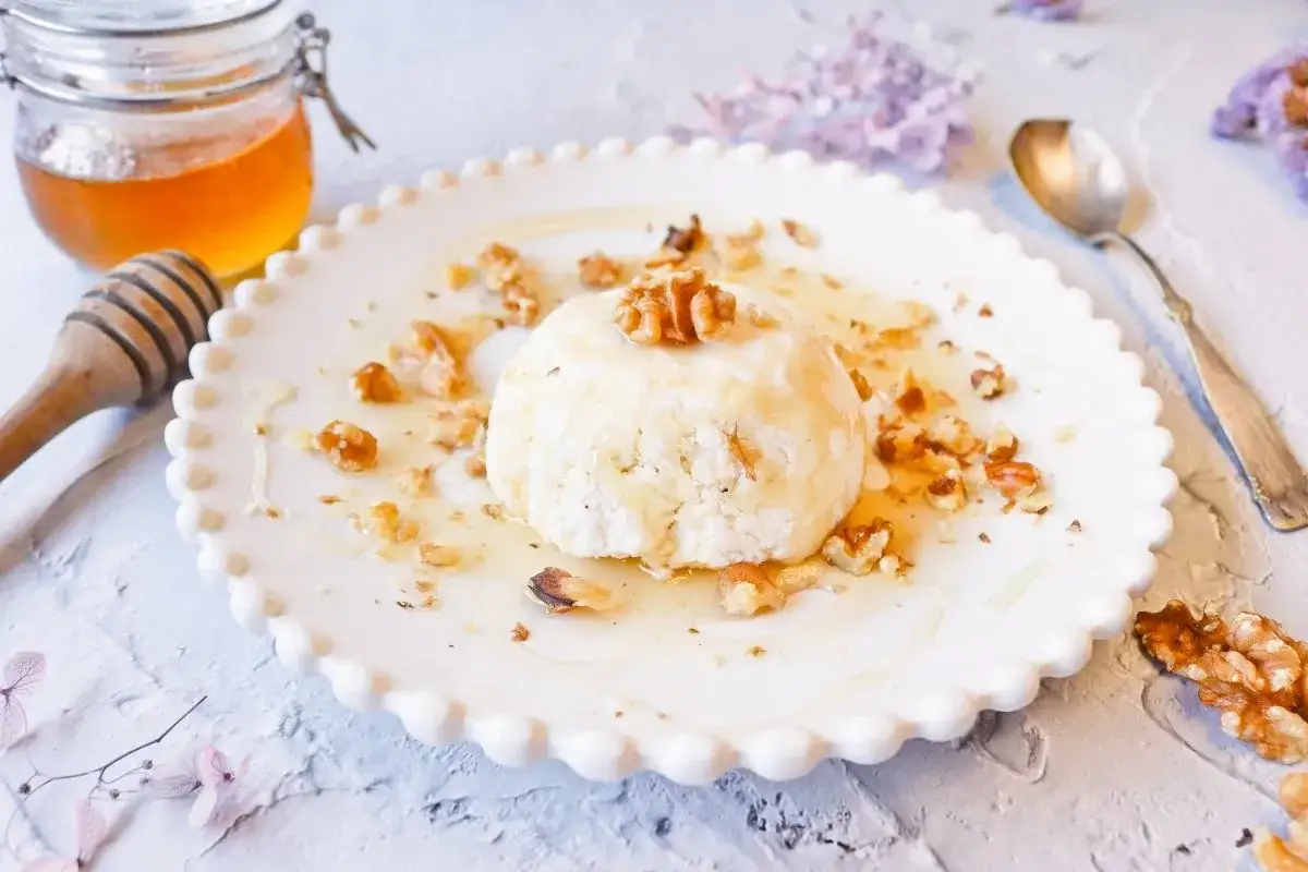 Delicioso postre de mel i mató con nueces y miel, servido en un plato blanco con borde festoneado.