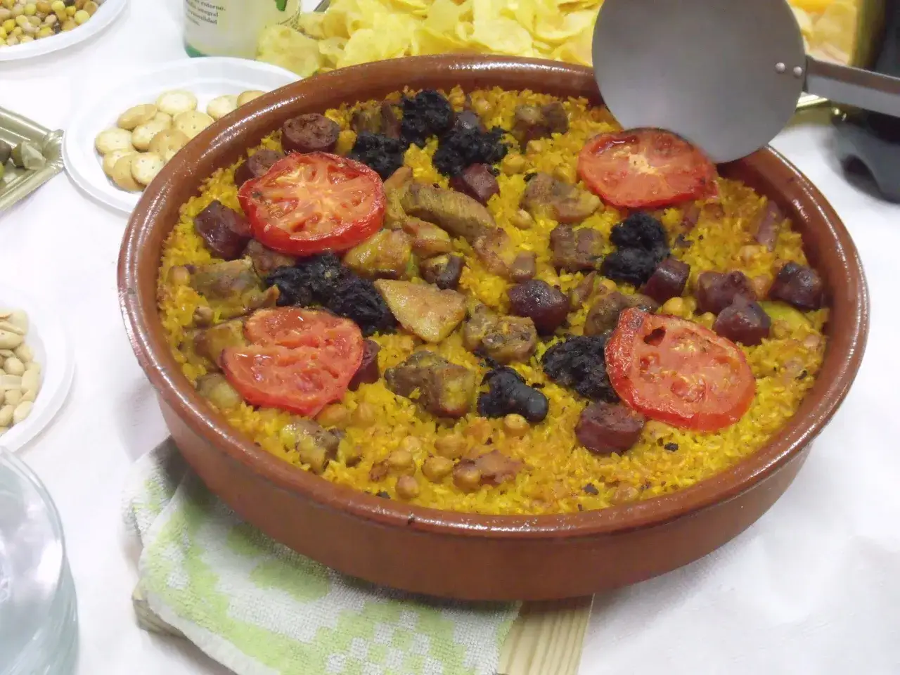 Arroz con aceitunas y trozos de carne, preparado en Thermomix, servido en paellera de barro con rodajas de tomate.