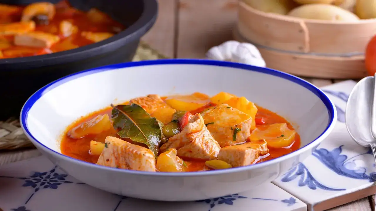 Un plato humeante de patatas con bonito, trozos de pescado tierno y patatas en una salsa roja sabrosa, decorado con hojas de laurel.