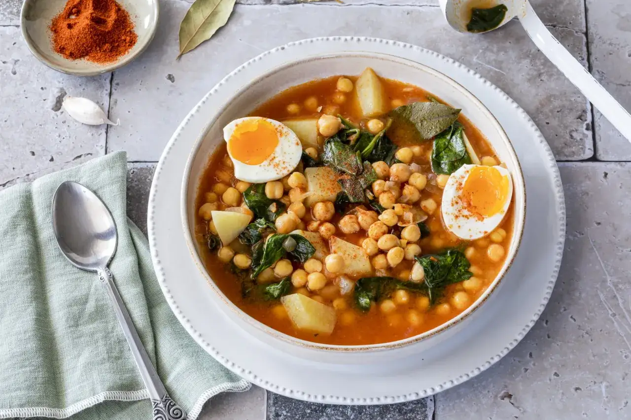 Un reconfortante potaje de garbanzos con patatas, espinacas y huevo duro, espolvoreado con piment&oacute;n.