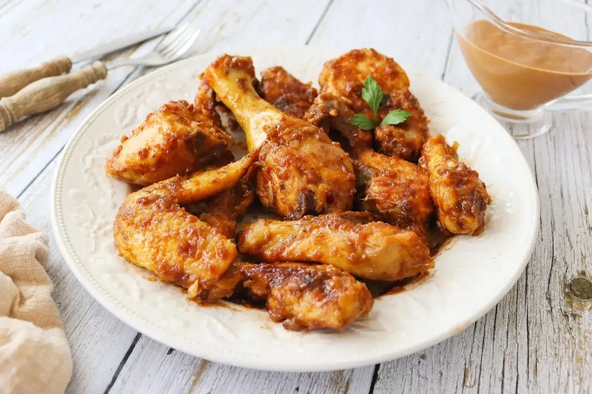 Sabroso pollo a la Coca Cola, jugoso y glaseado, servido en un plato blanco con una salsa aparte.