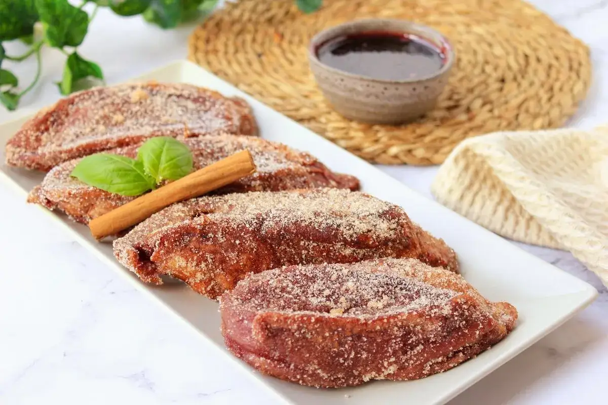 Torrijas de vino espolvoreadas con azúcar y canela, decoradas con una hoja verde y una rama de canela.