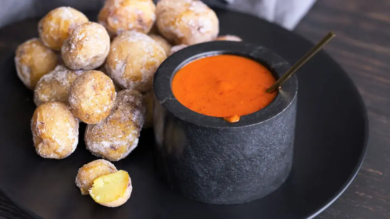 Papas arrugadas cubiertas de sal, listas para ser sumergidas en una salsa roja picante.