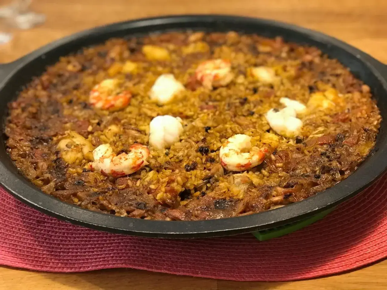 Arroz de tamboril con gambas y trozos blancos de pescado, servido en una paellera negra sobre una alfombrilla roja.