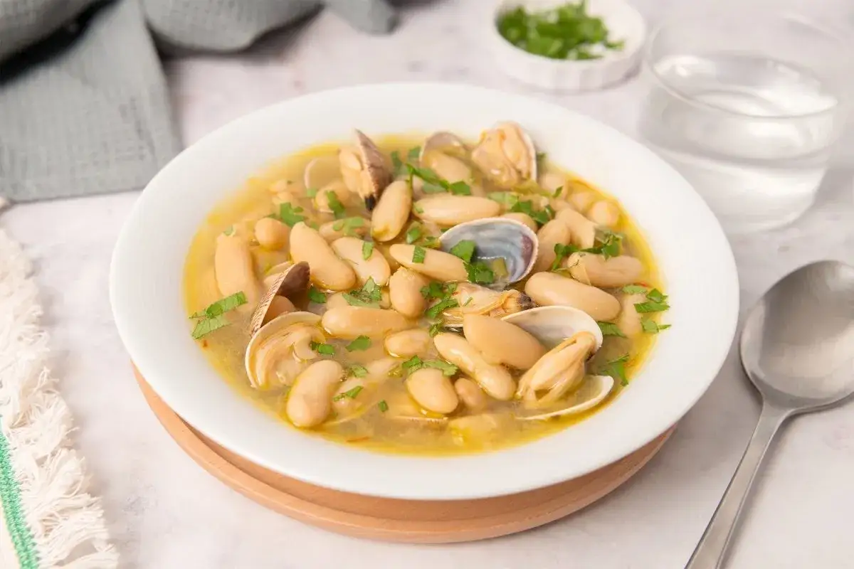 Plato de habichuelas con almejas, un guiso reconfortante con jud&iacute;as blancas tiernas y almejas frescas, espolvoreado con perejil picado.
