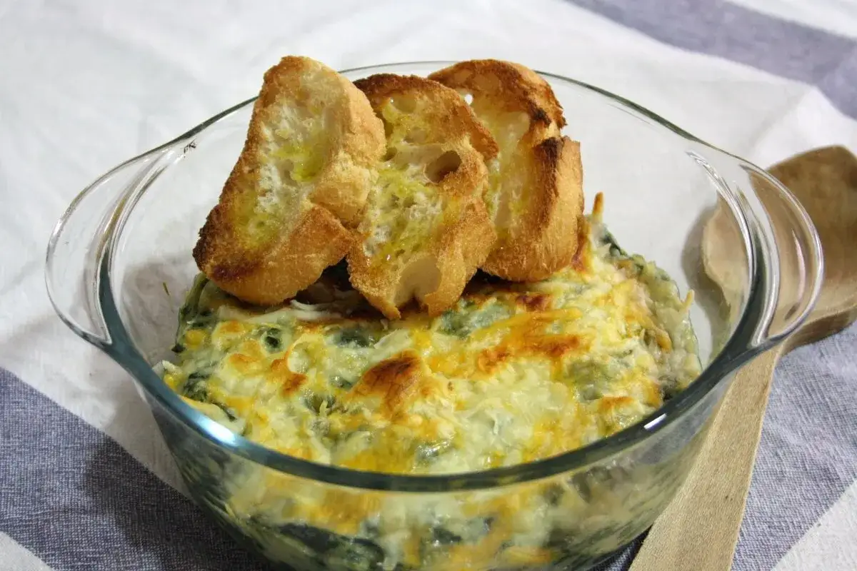 Delicioso plato de espinacas a la crema gratinadas, servido en una fuente de cristal y coronado con tostadas de pan.