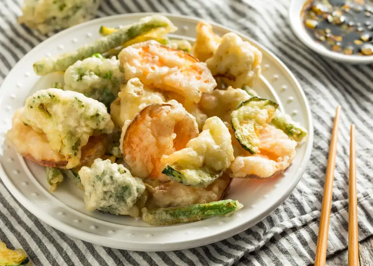 Deliciosa tempura de verduras y camarones, crujiente y dorada, lista para ser disfrutada con salsa.