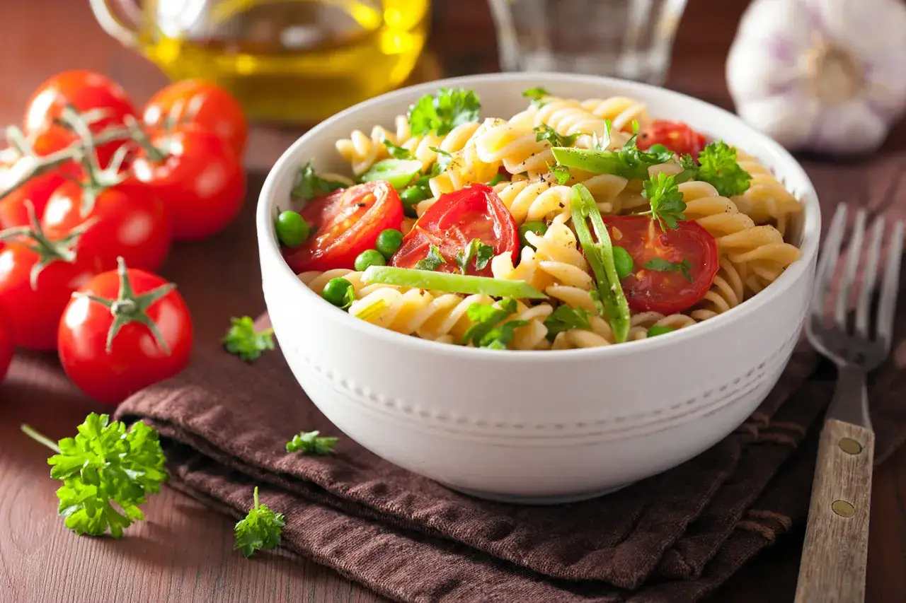 Un plato de pasta con verduras frescas: tomates cherry, guisantes y perejil, servido en un cuenco blanco.