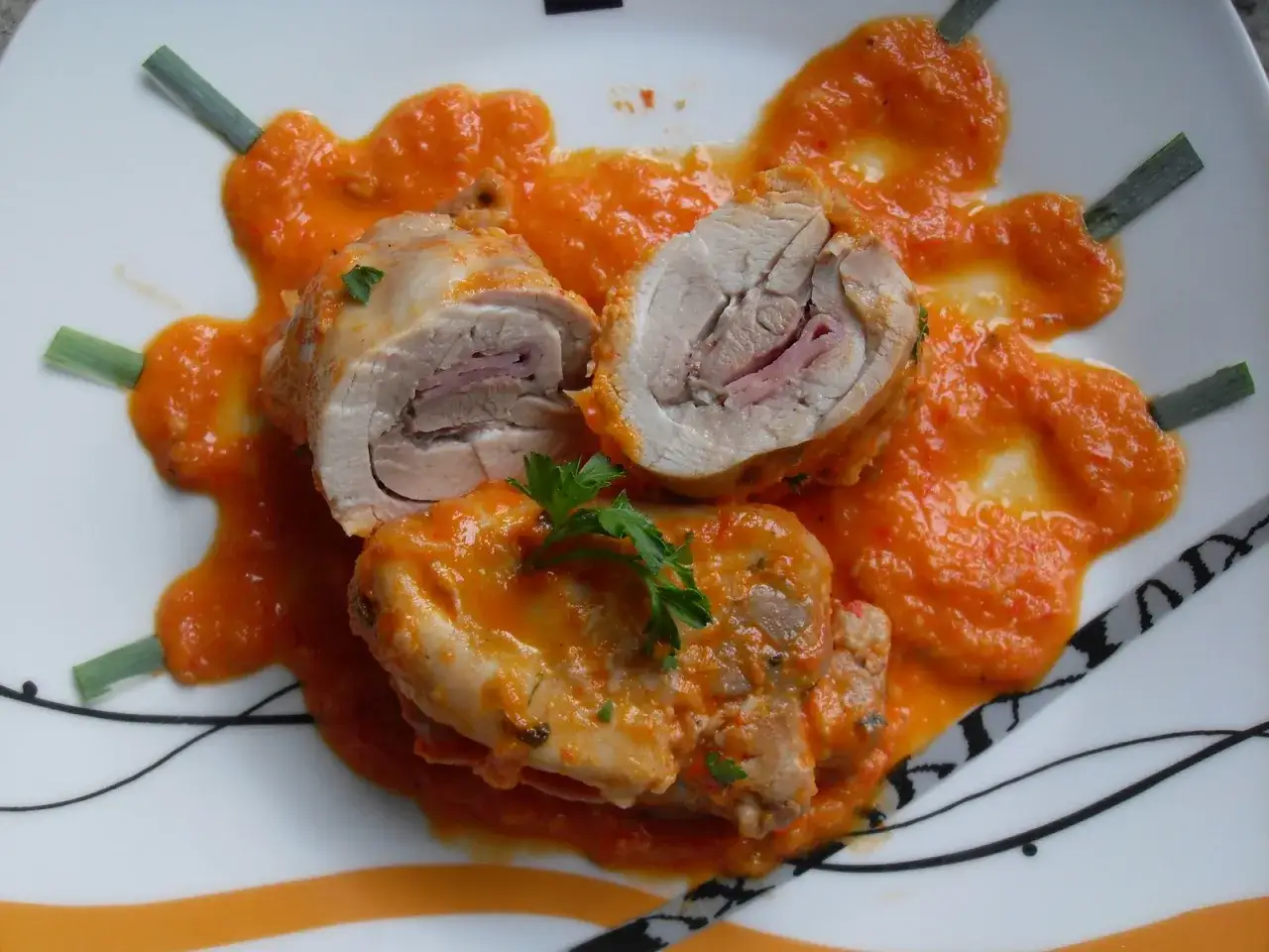 Contramuslos de pollo Thermomix enrollados con jam&oacute;n, cubiertos de salsa de pimientos rojos y decorados con perejil y cebolleta.