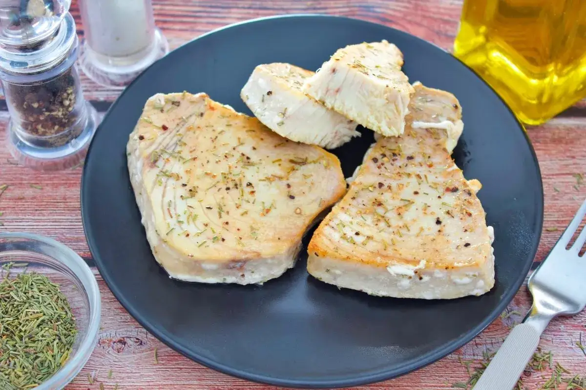 Filetes de pez espada bonito a la plancha, sazonados con hierbas y especias, servidos en un plato negro.