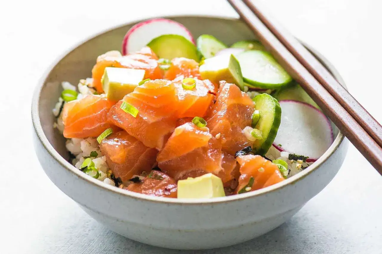 Un delicioso poke de salm&oacute;n fresco con aguacate, pepino y r&aacute;bano, servido sobre arroz blanco.