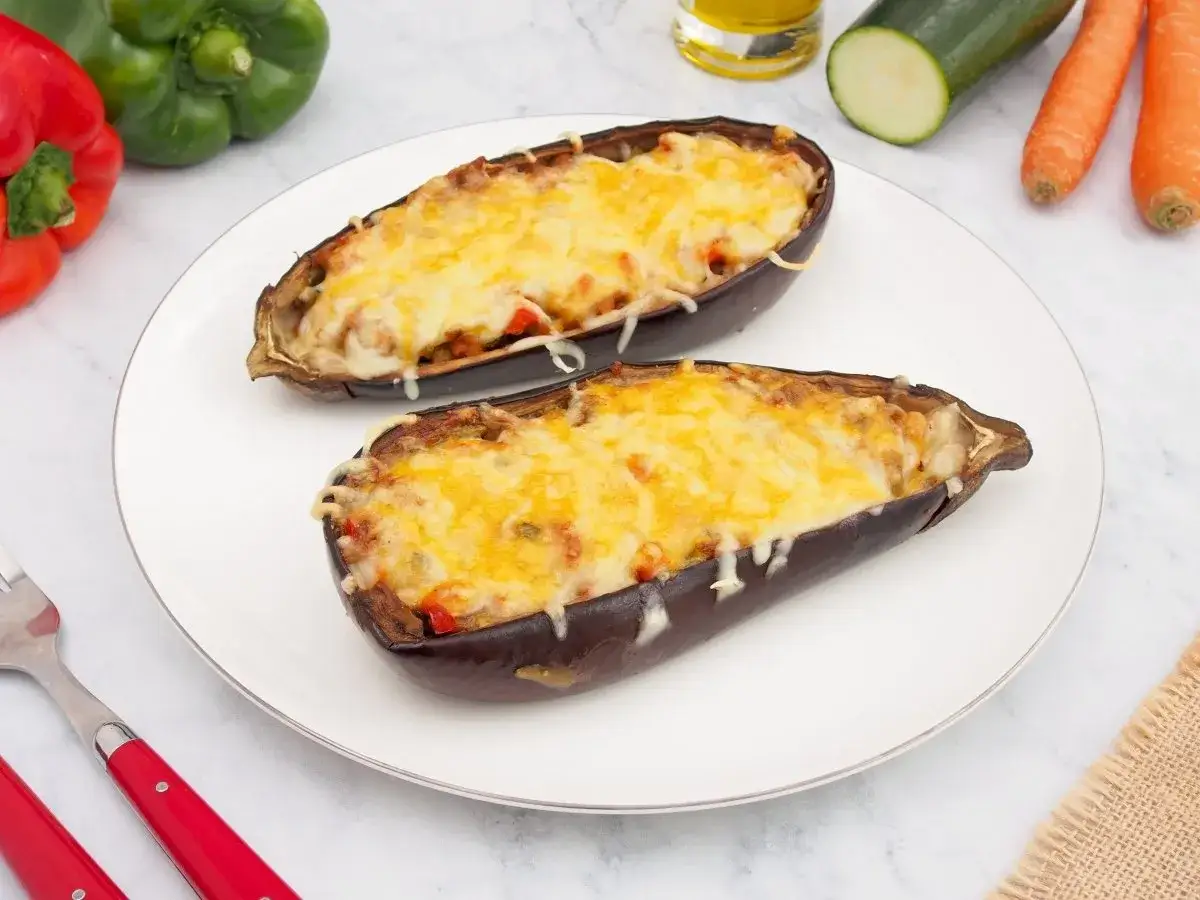 Dos mitades de berenjenas rellenas de verduras y gratinadas con queso, listas para disfrutar.