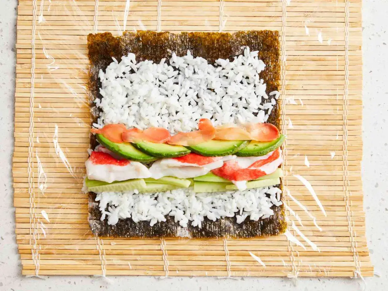Preparando los ingredientes para saber como hacer sushi: alga nori, arroz, aguacate, pepino y surimi sobre una esterilla de bamb&uacute;.