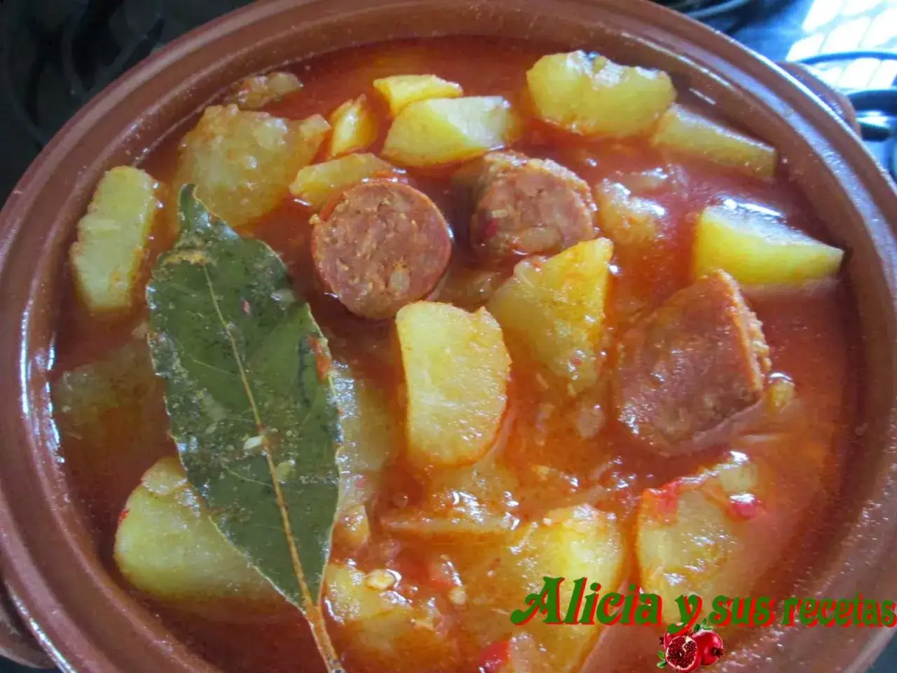 Un cuenco de barro con patatas a la riojana, trozos de chorizo y una hoja de laurel.