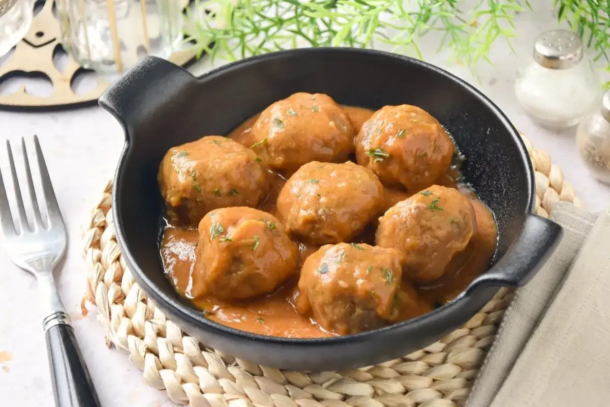 Sabrosas albondigas en salsa casera, servidas en una cazuela negra, listas para disfrutar con un tenedor.
