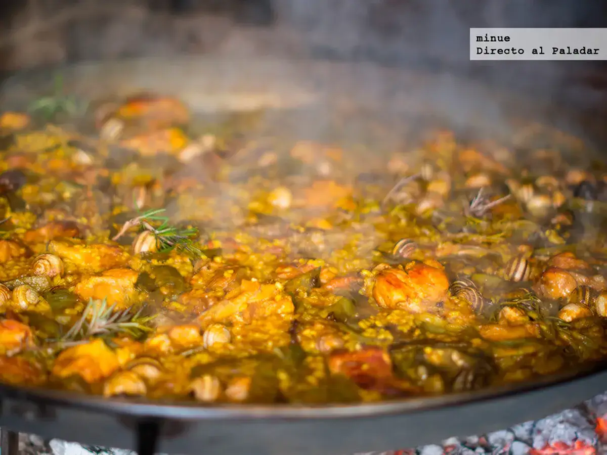 Una humeante paella valenciana, con caracoles y romero, burbujea en una paellera sobre brasas.