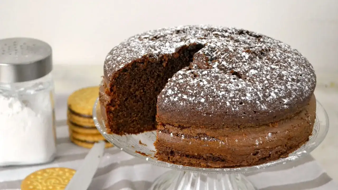 Bizcocho de chocolate espolvoreado con az&uacute;car glas, acompa&ntilde;ado de galletas Pr&iacute;ncipe y un azucarero.