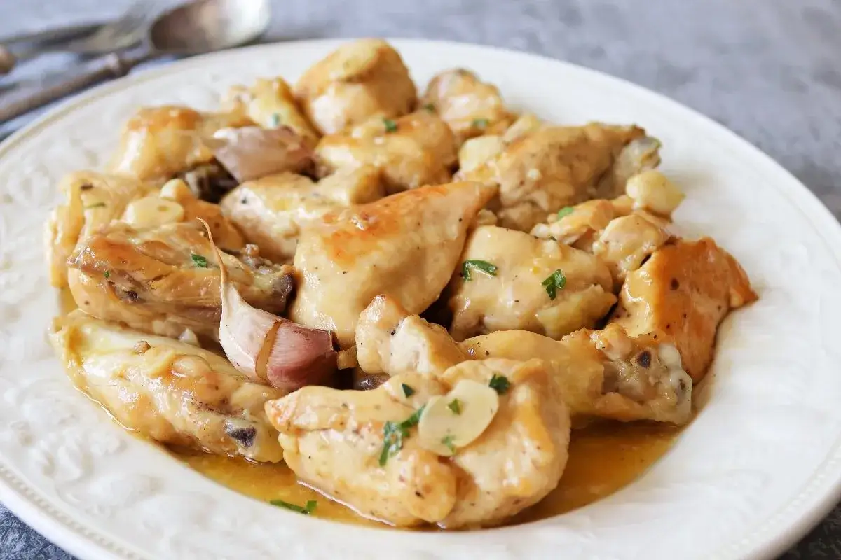 Sabroso pollo al ajillo servido en un plato blanco, con trozos de pollo dorados y ajos enteros.