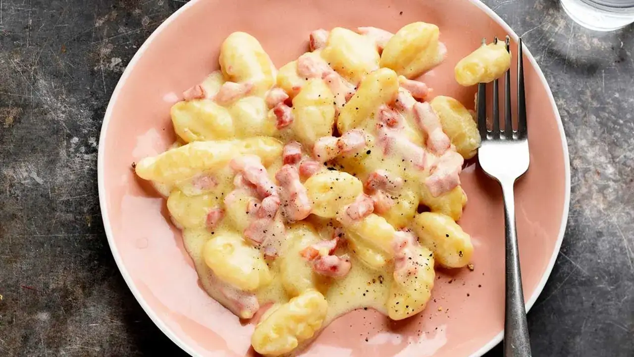 &Ntilde;oquis a la carbonara cremosos y deliciosos, cubiertos con trozos de panceta y pimienta negra, servidos en un plato rosa.