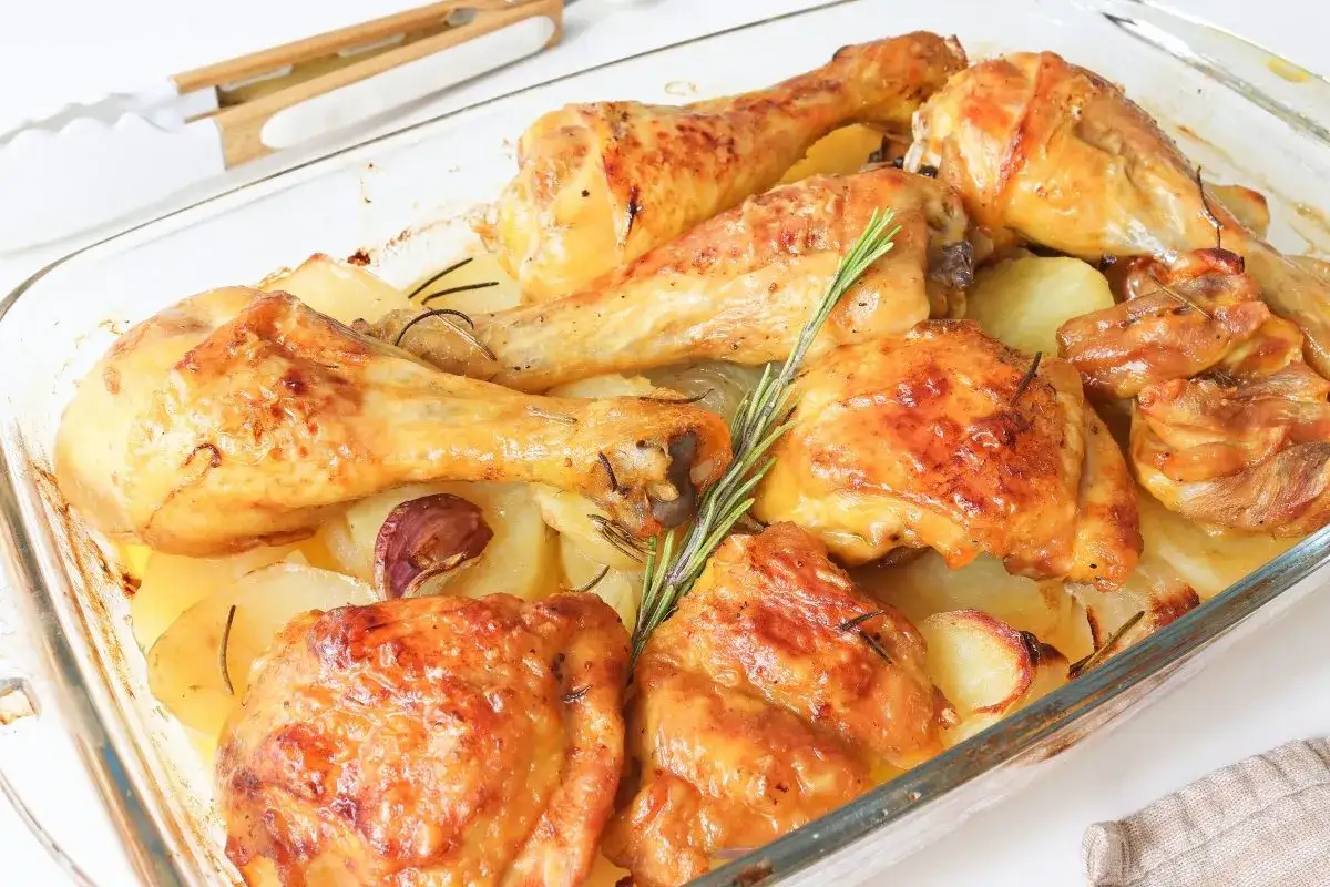 Pollo al horno con patatas, ajo y romero en una fuente de vidrio. Un plato casero listo para servir.