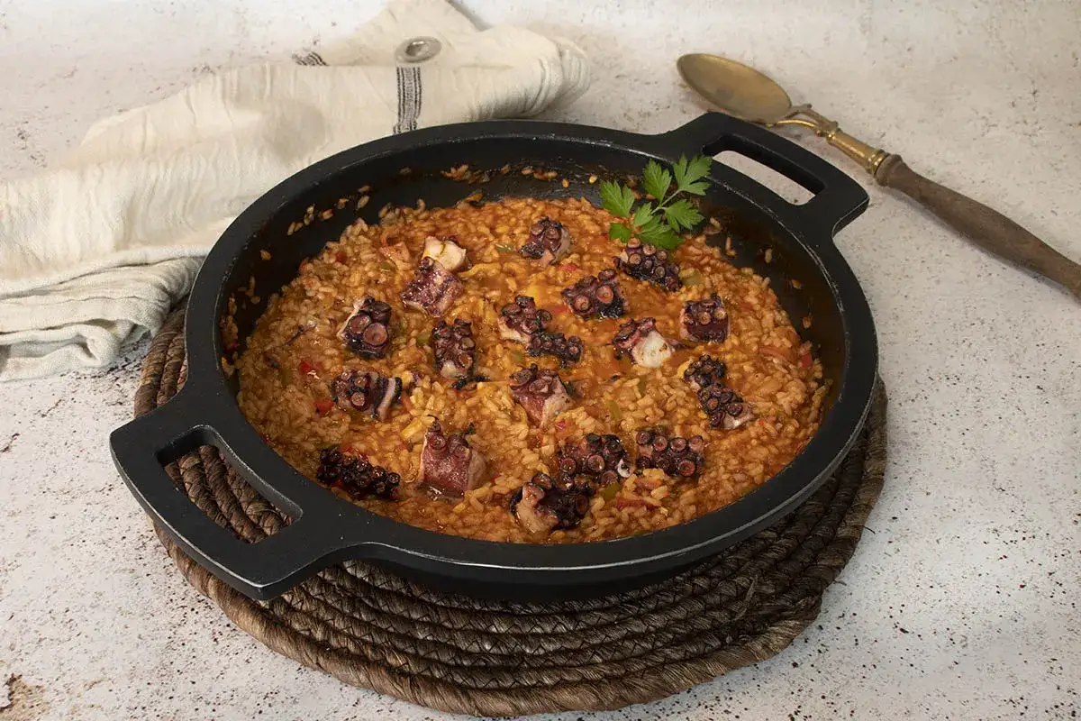 Delicioso arroz con pulpo en paellera, adornado con perejil fresco. Un plato que huele a mar y sabor.