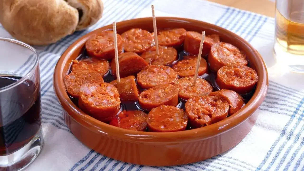 Tapa de chorizo a la sidra, servido en cazuela de barro con palillos. Acompa&ntilde;ado de pan y copas de vino.