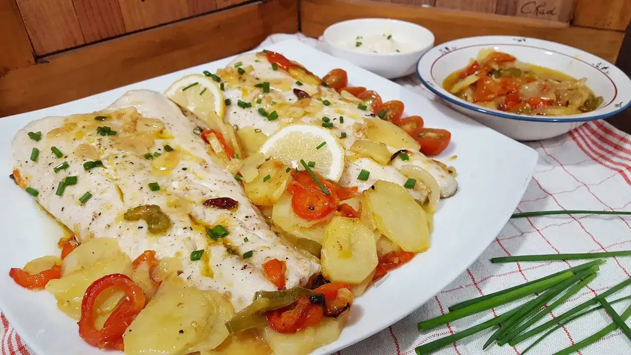 Deliciosa merluza al horno con patatas, pimientos y tomates. Un plato principal perfecto para cualquier ocasi&oacute;n.