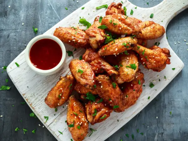 Deliciosas alitas de pollo fritas, doradas y crujientes, servidas con salsa y perejil picado.