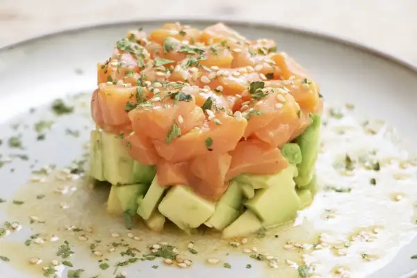 Delicioso tartar de salmón fresco con aguacate, espolvoreado con sésamo y perejil. Una explosión de sabor y color.