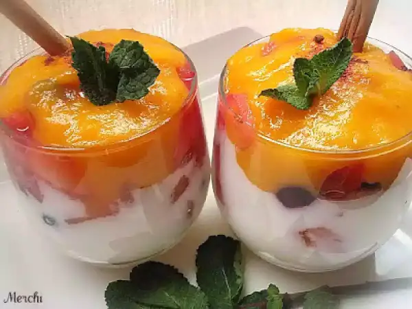 Dos copas de cristal con capas de yogur blanco, trozos de fruta roja y un delicioso mousse de mango coronado con menta y canela.