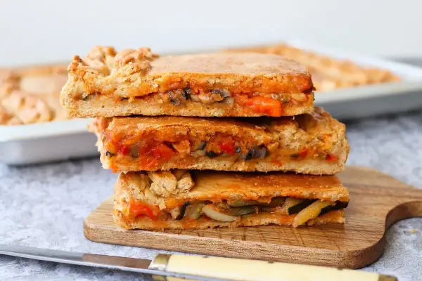 Tres porciones de empanada de verduras apiladas, con relleno de pimientos, calabacín y tomate.