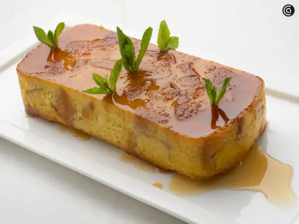 Pan de Calatrava, un postre dorado con caramelo líquido y hojas de menta, servido en una bandeja blanca.