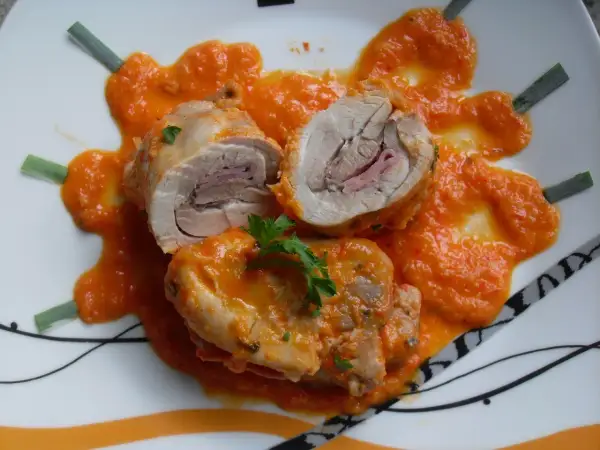 Contramuslos de pollo Thermomix enrollados con jamón, cubiertos de salsa de pimientos y decorados con perejil y cebolleta.