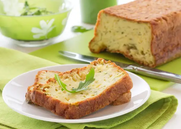 Rebanadas de un delicioso pastel de calabacín, esponjoso y dorado, servidas en un plato blanco con una hoja verde.