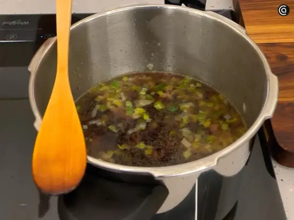 Olla express con alubias y verduras, lista para el tiempo de cocción. Una cuchara de madera descansa a un lado.
