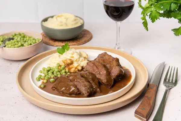 Carrilleras de ternera en salsa, un plato reconfortante que evoca la auténtica receta de la abuela, acompañado de puré de patatas y guisantes.