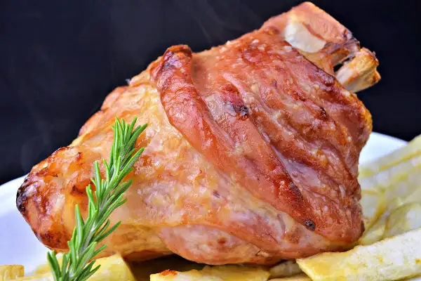 Codillo de cerdo asado, dorado y jugoso, servido con patatas fritas y una ramita de romero.