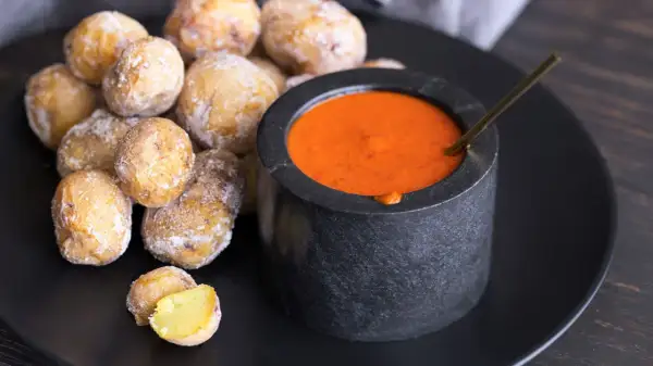 Papas arrugadas cubiertas de sal marina, listas para ser sumergidas en una salsa roja picante.