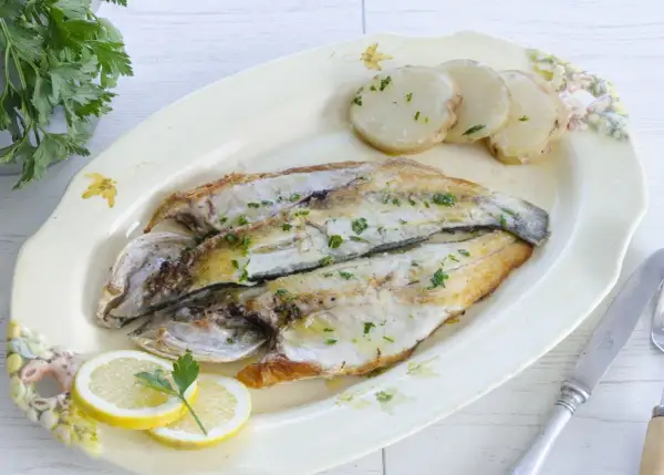 Lubina a la plancha, dorada y jugosa, servida con patatas y rodajas de limón. Un plato sencillo y delicioso.