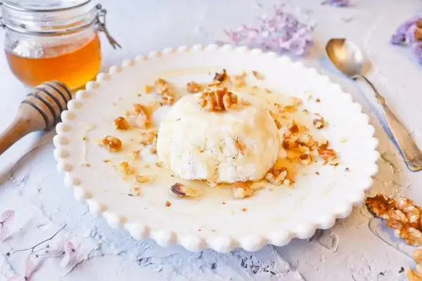 Delicioso postre de mel i mató con nueces y miel, servido en un plato blanco con borde festoneado.